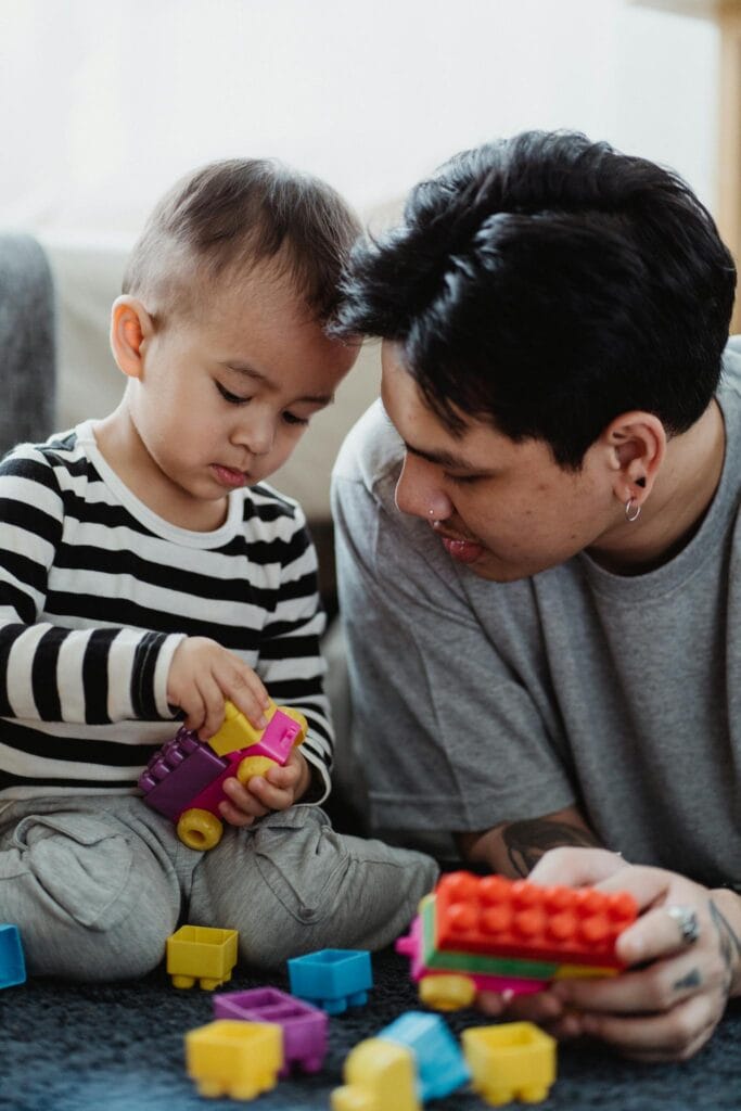 Father and toddler son bonding through play with colorful building blocks.
